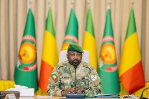 Un officier militaire en uniforme, assis devant des drapeaux maliens, lors d'une conférence.