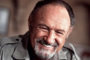 Un homme avec une barbe grise souriant joyeusement, portant une chemise décontractée.