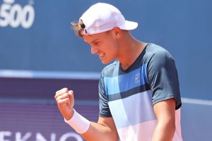 Un jeune joueur de tennis célèbre une victoire avec un poing levé, montrant sa joie et sa détermination.