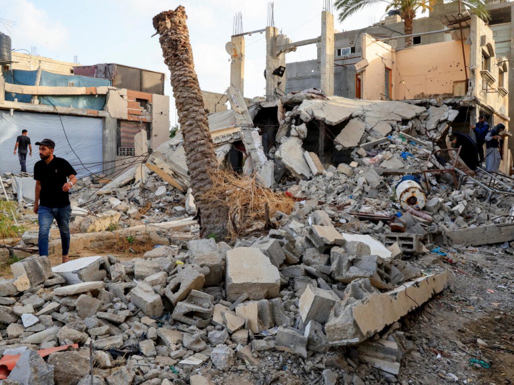 Un homme marche à travers les décombres d'immeubles détruits, tandis que d'autres inspectent les dégâts dans un quartier touché.