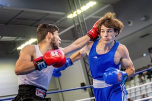Combat de boxe::Un boxeur en bleu reçoit un coup de poing d'un adversaire en blanc dans un ring, capturant l'intensité du match.