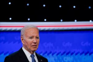 Joe Biden s'exprime lors d'un débat avec un éclairage de scène et un fond coloré.