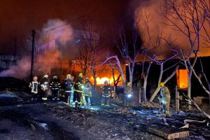 Des pompiers combattent un incendie dans un bâtiment en feu, avec des flammes visibles et de la fumée dans une nuit sombre.