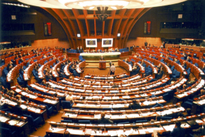 Assemblée parlementaire : vue panoramique d'une session en cours avec des délégués dans une salle colorée et arrondie.
