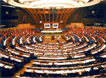 Assemblée parlementaire : vue panoramique d'une session en cours avec des délégués dans une salle colorée et arrondie.