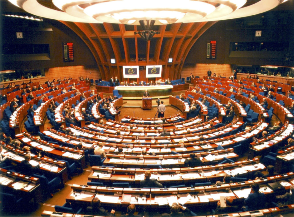 Assemblée parlementaire : vue panoramique d'une session en cours avec des délégués dans une salle colorée et arrondie.